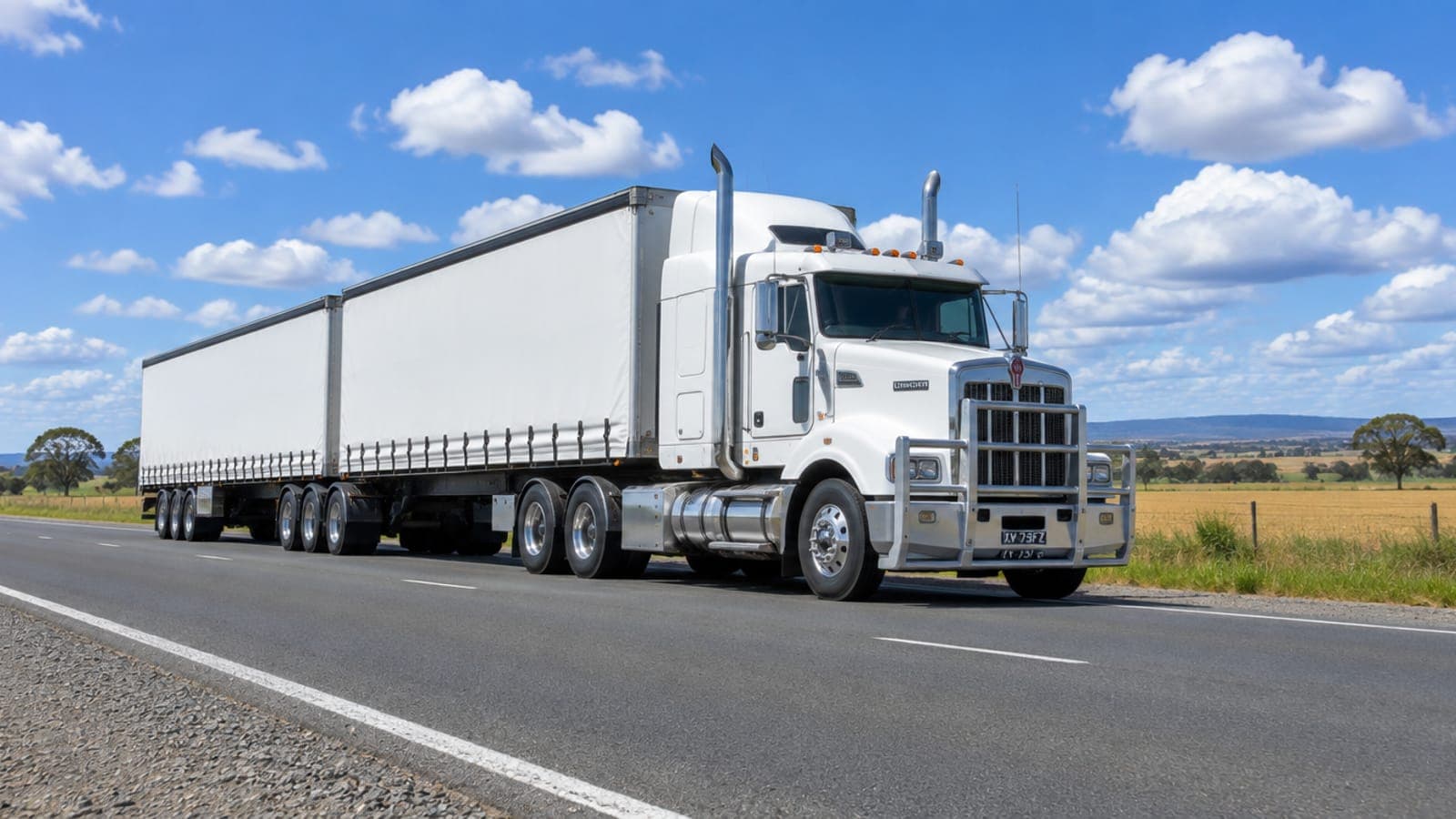A white B-double prime mover on a country highway under a blue sky
